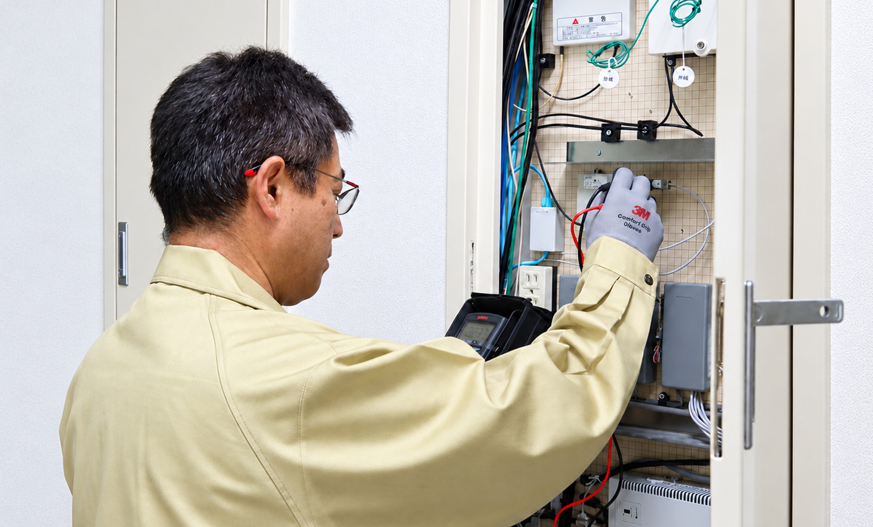 作業着の技術者が配電盤を点検している様子